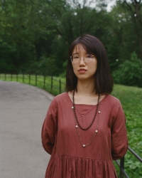 A woman in a dark red dress stands in front of a patch of green grass.