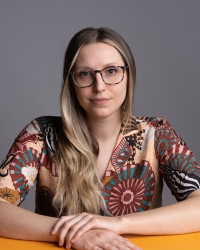 Woman with long blonde hair, glasses, and colorful patterned shirt