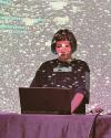 A female with bob haircut uses laptop to make live coding visuals that are projected on the wall behind