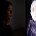 Image of Anaid Bohor, performer, controlling a virtual Avatar. Standing in front of a screen. 